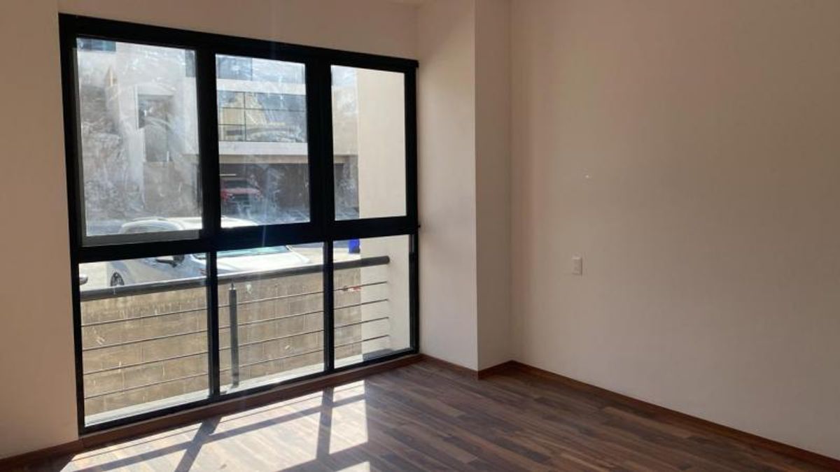 Habitación vacía con piso de madera, paredes claras y gran ventanal con marco negro