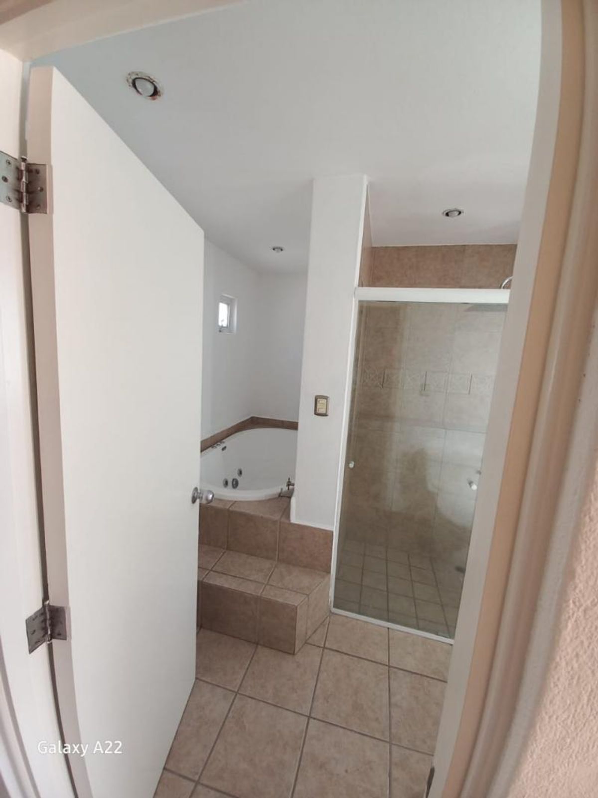 Baño con tina de hidromasaje elevada, ducha con cancel de cristal y piso cerámico