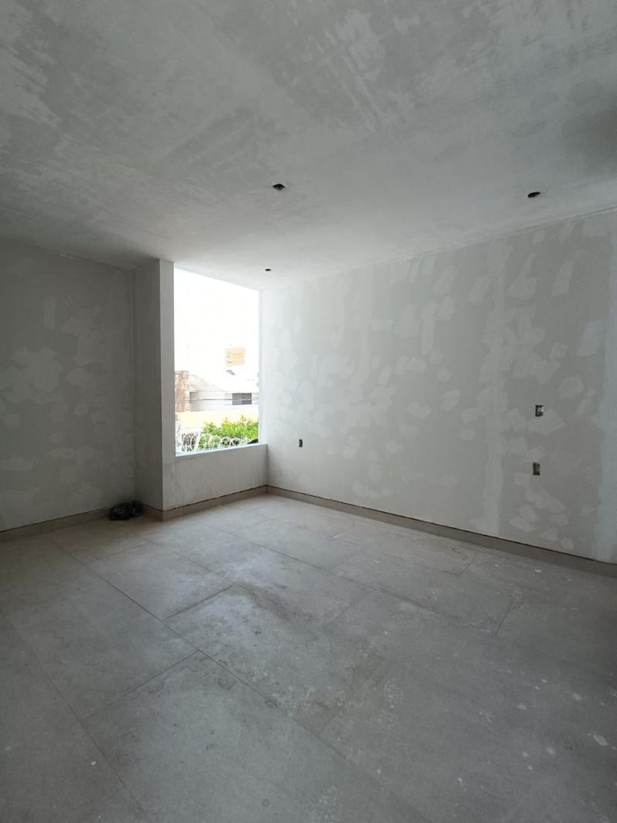 Habitación en proceso de acabado con piso cerámico gris, paredes empastadas y ventanal exterior