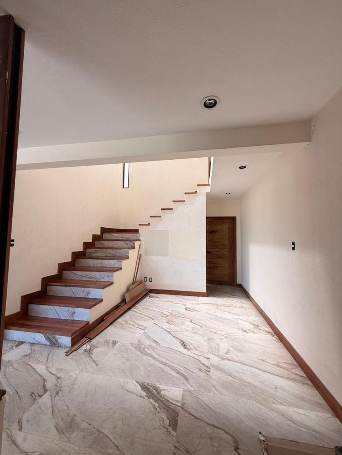 Escalera interior con peldaños de madera, piso tipo mármol y puerta al fondo