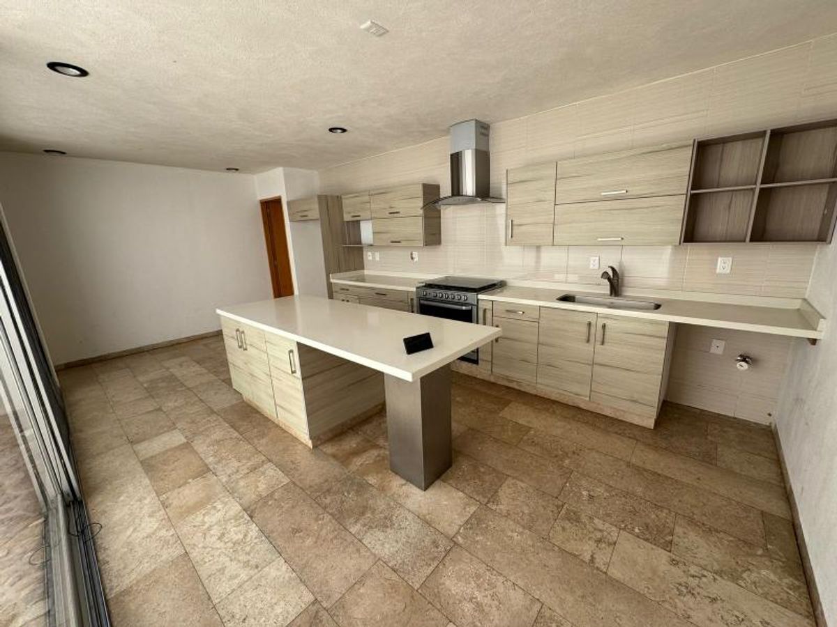 Cocina con isla central blanca, gabinetes de madera clara, campana extractora y piso cerámico