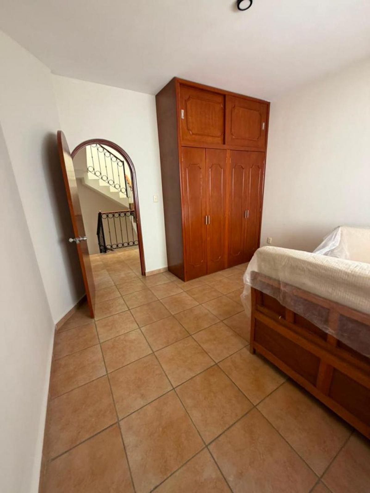Habitación con piso de azulejo, clóset alto de madera, paredes blancas y puerta arqueada