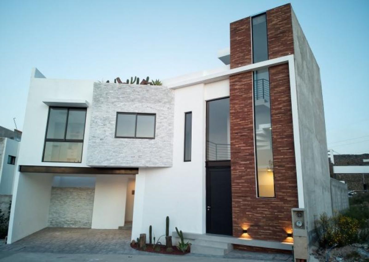 Fachada moderna blanca de dos niveles con muro de piedra café, ventanales y cochera