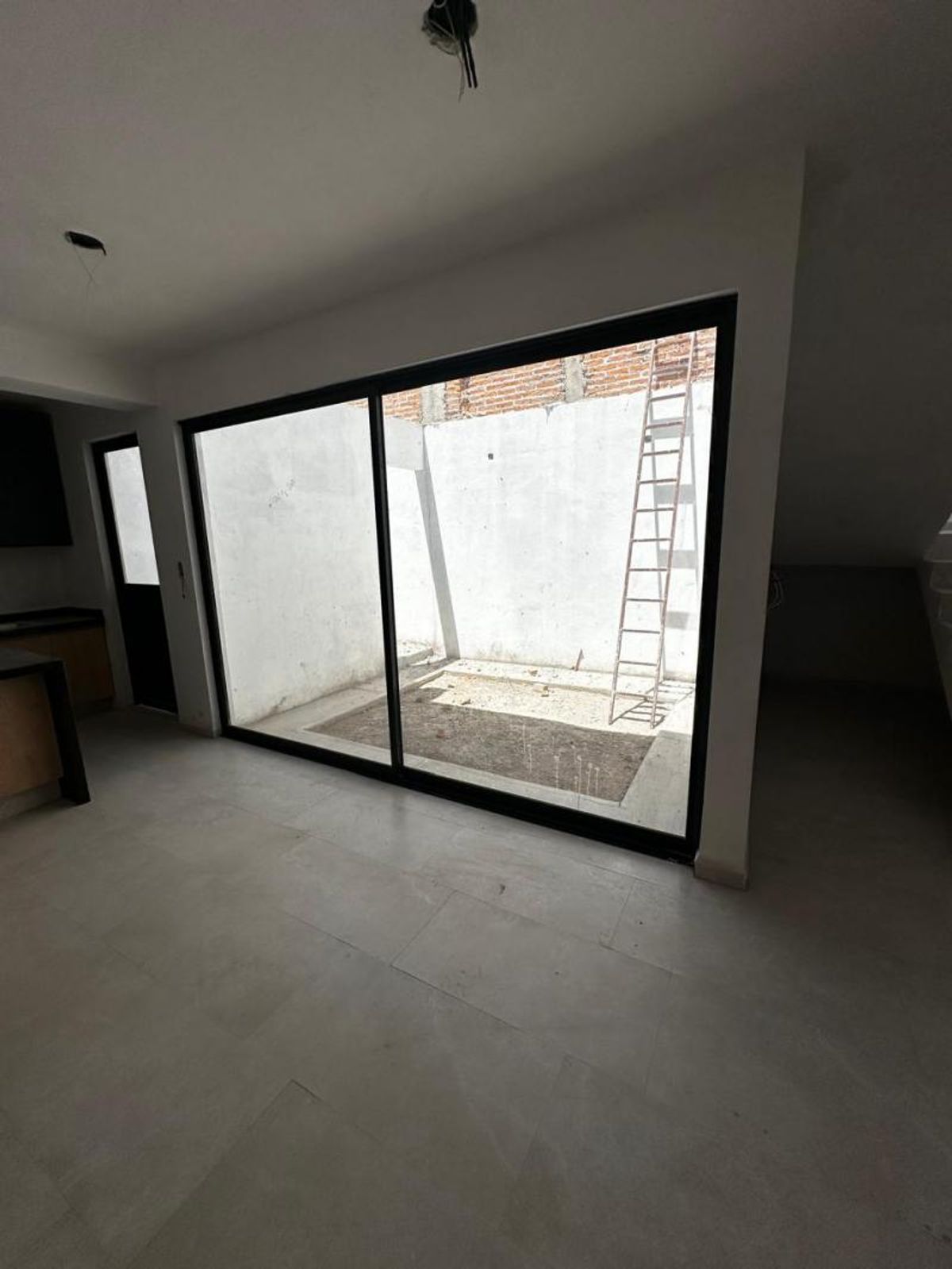 Estancia con piso cerámico claro y gran ventanal de marco negro hacia patio