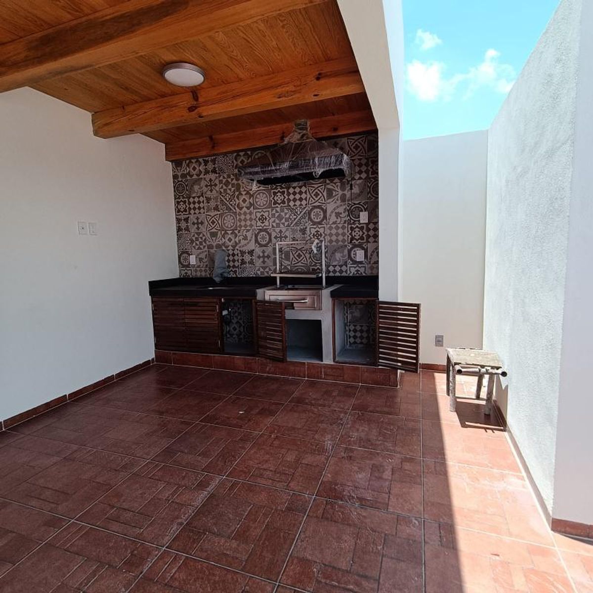 Terraza cubierta con piso de cerámica, techo de madera y barra con asador integrado