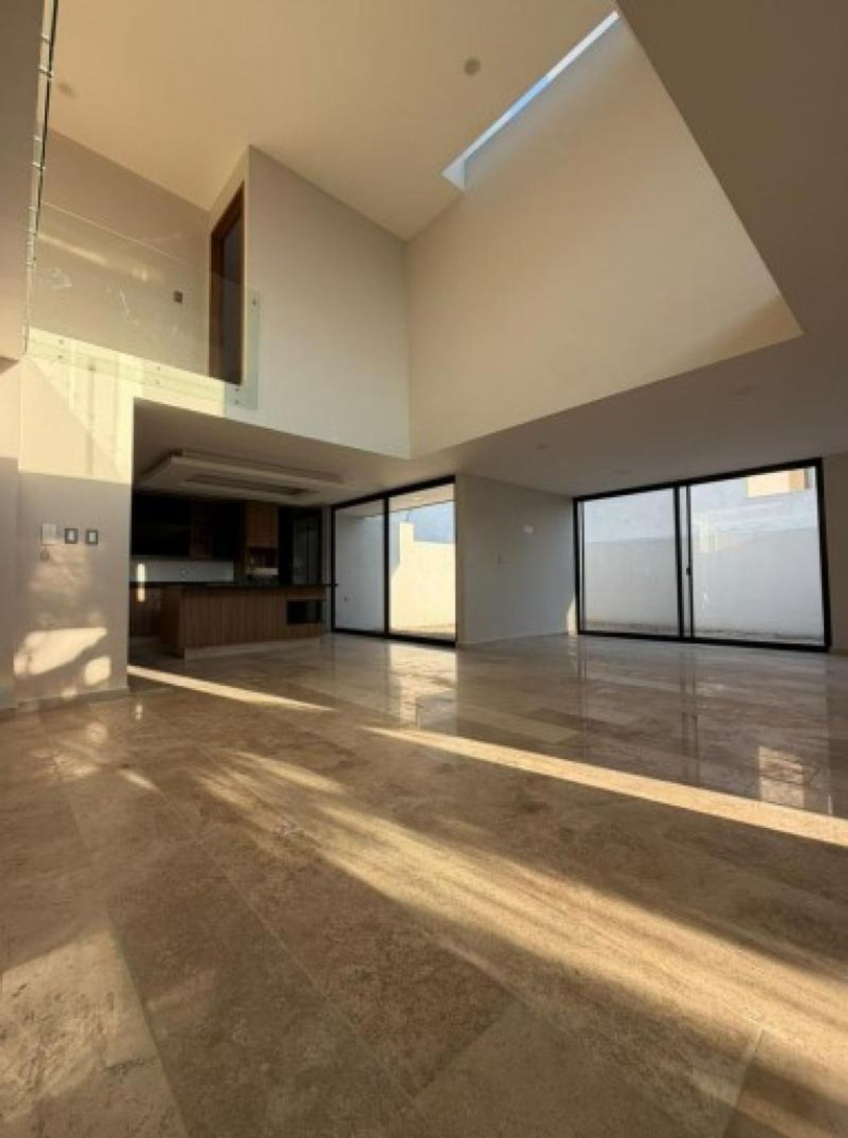 Espacio abierto con doble altura, pisos de mármol brillante y ventanales corredizos al patio