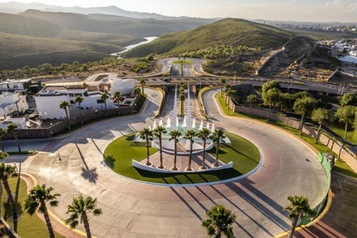Glorieta circular pavimentada con palmeras, fuentes de agua y esculturas blancas rodeada de colinas
