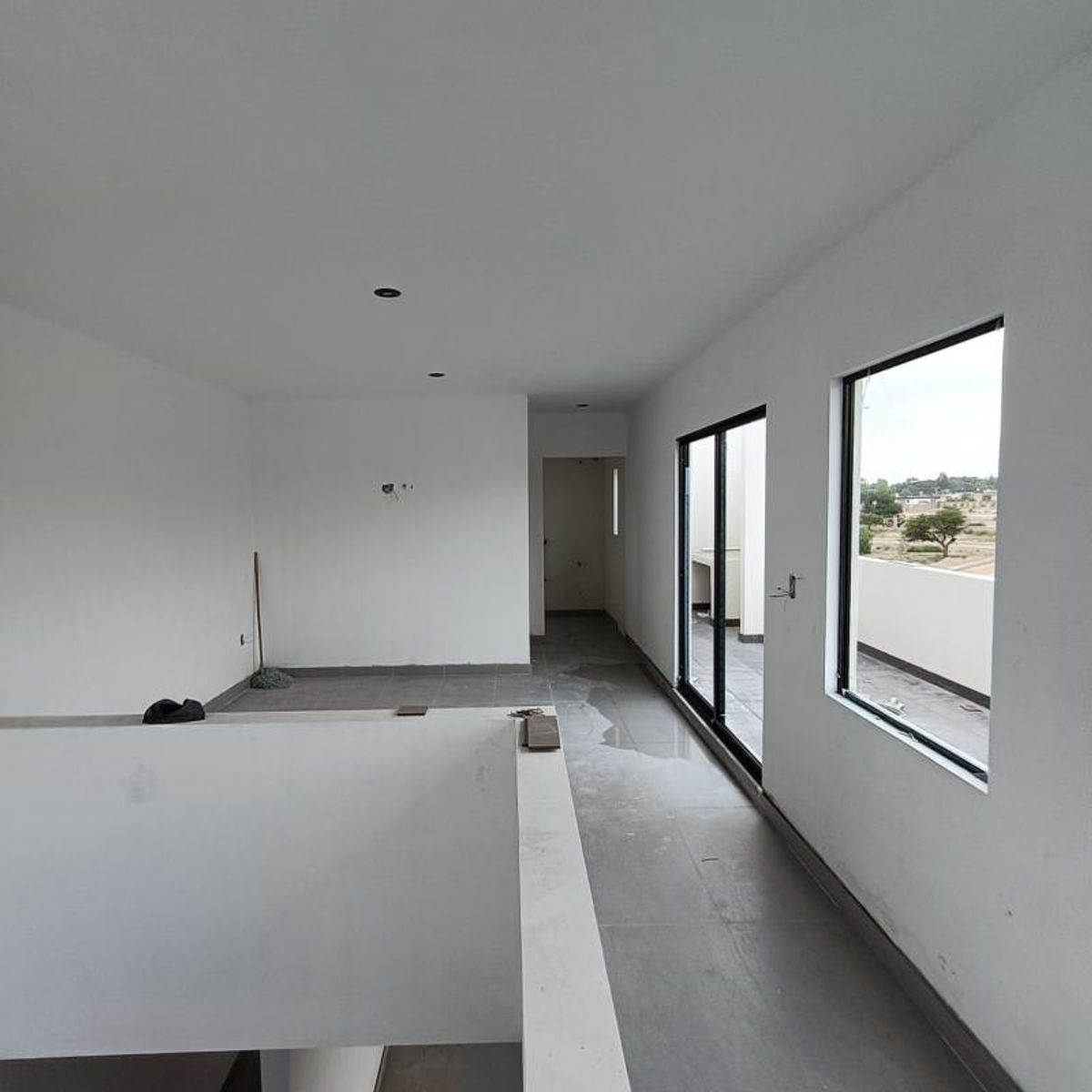 Espacio amplio con muros blancos, piso gris y ventanales de marcos negros
