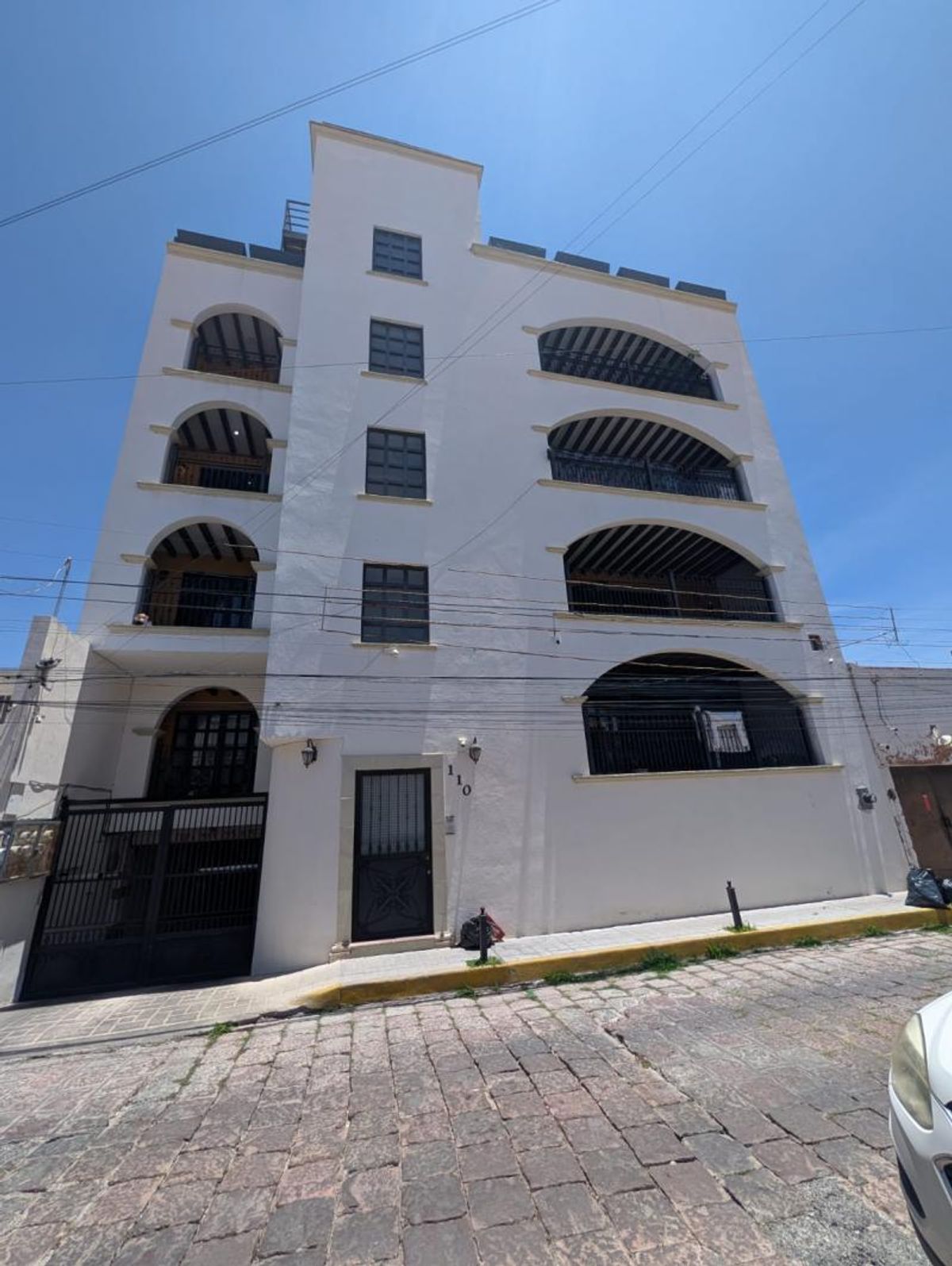 Fachada de edificio blanco de varios pisos con balcones arqueados sobre calle empedrada