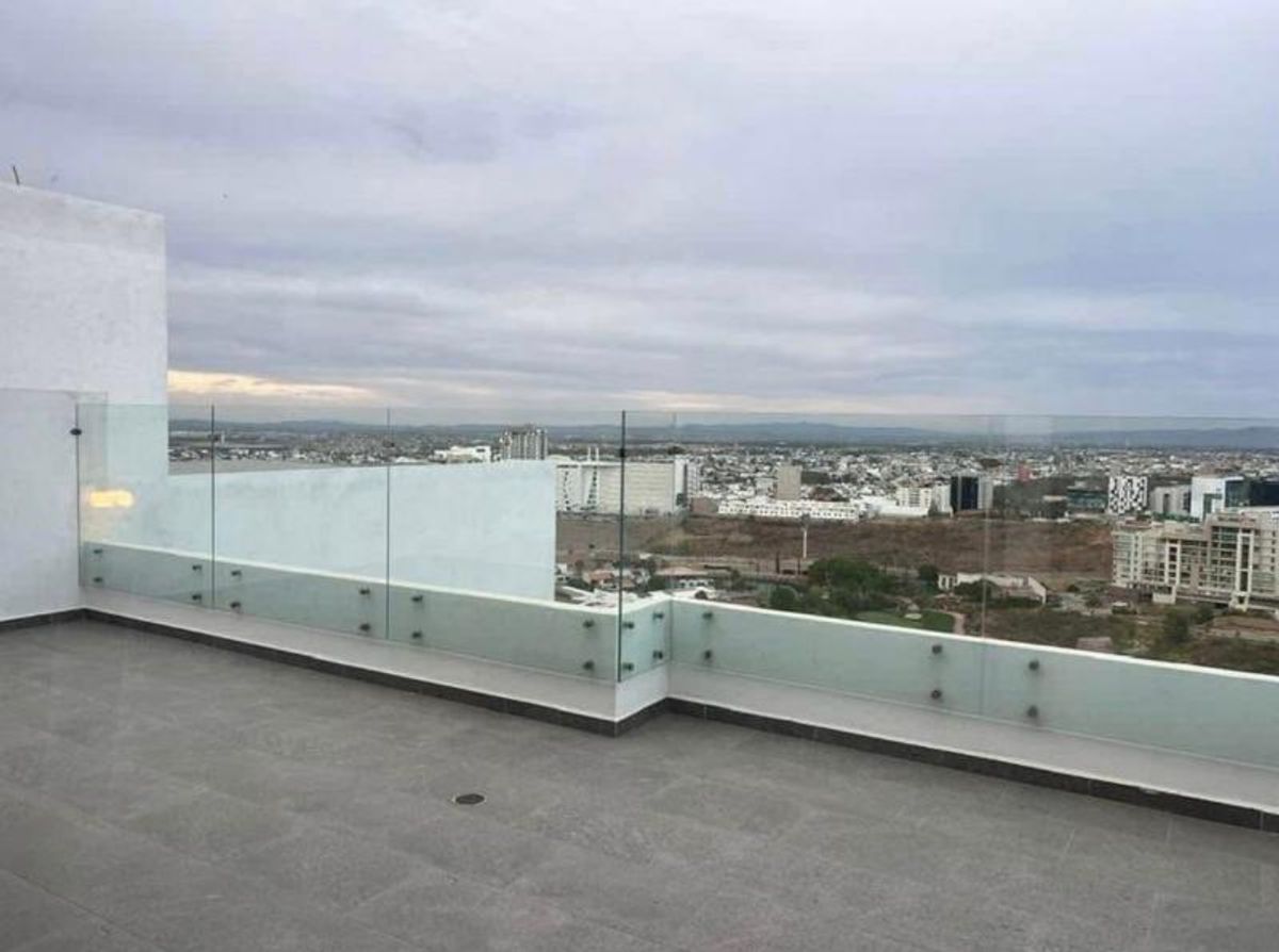 Terraza exterior con piso gris, barandal de cristal y vista panorámica de la ciudad
