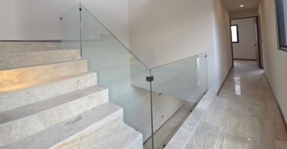Escalera y pasillo con pisos de mármol claro y barandal de cristal transparente