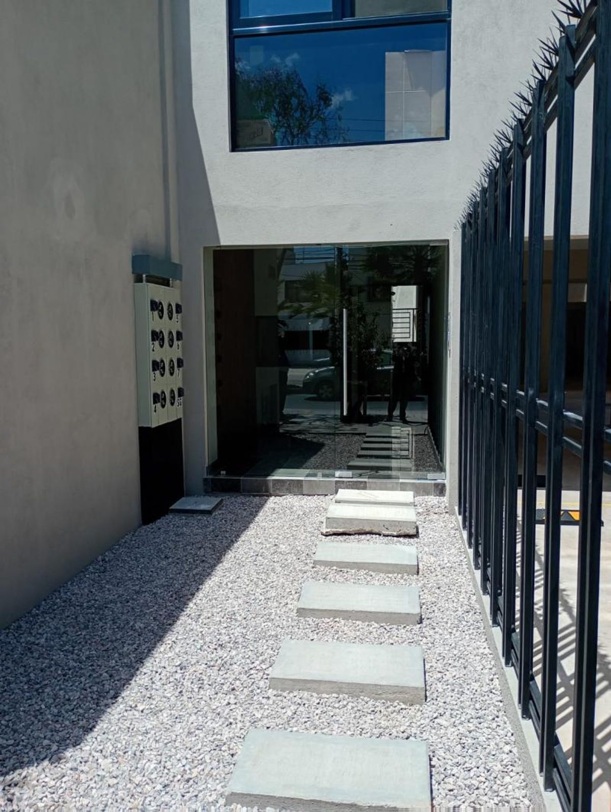 Acceso exterior con camino de losas de concreto sobre grava hacia puerta de vidrio