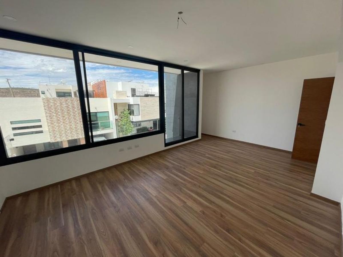 Habitación vacía con piso laminado de madera, paredes blancas y grandes ventanales de marco negro