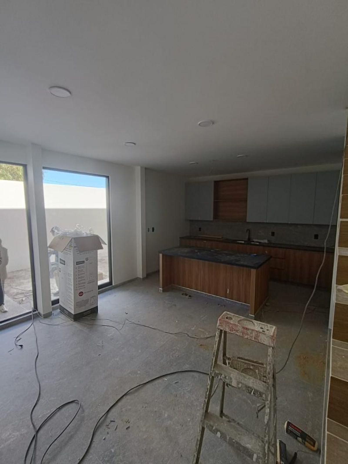 Cocina con isla de madera, gabinetes superiores grises, ventanales e iluminación empotrada