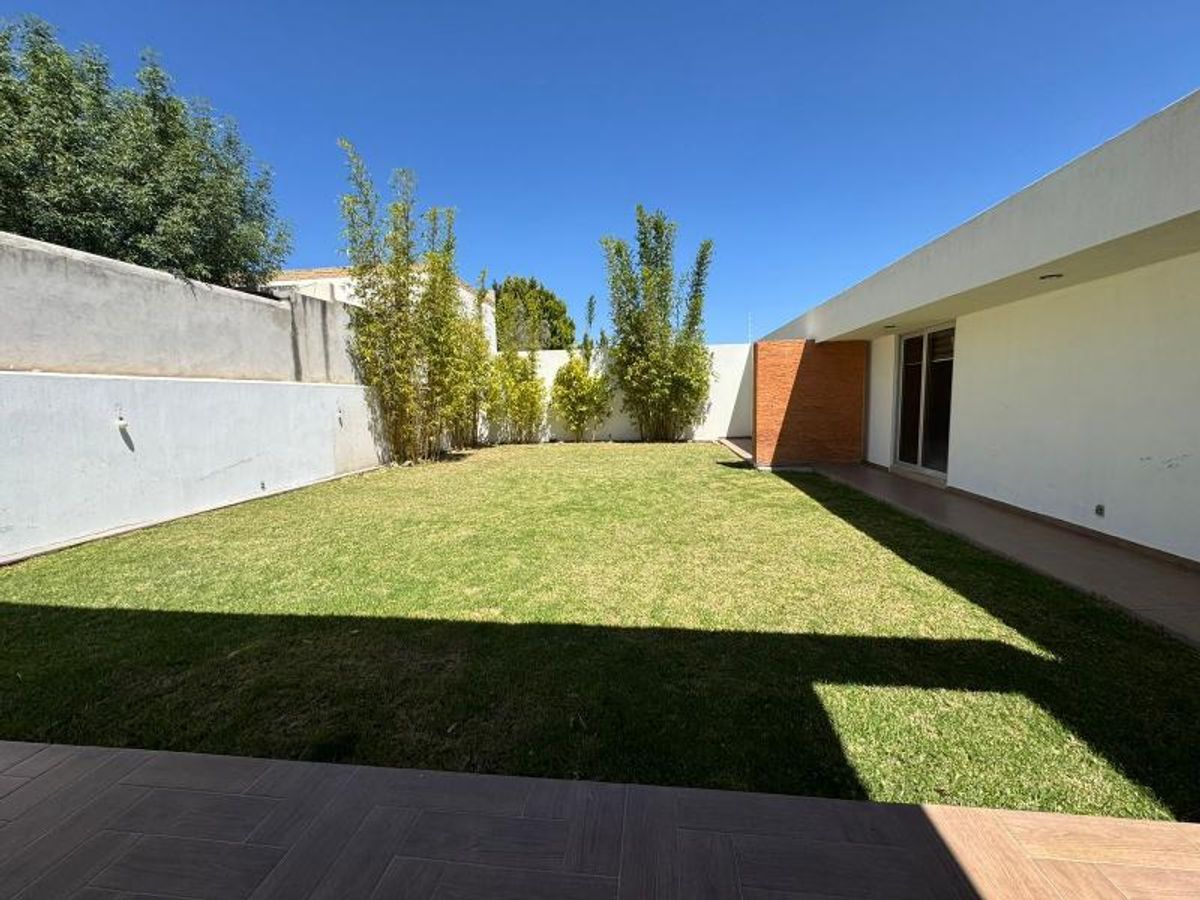 Jardín con pasto verde, bambúes al fondo, terraza con piso cerámico y muros blancos