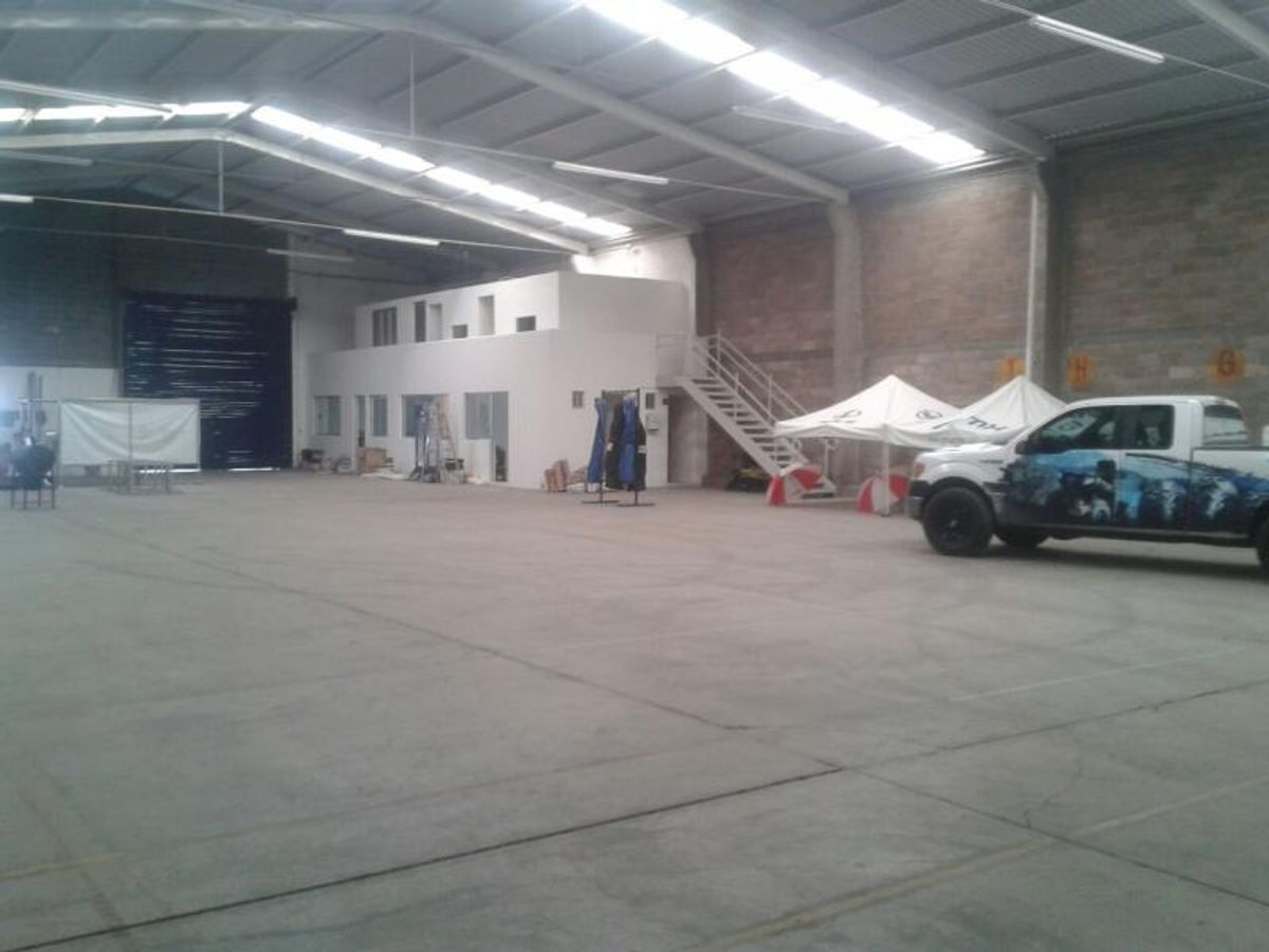 Interior de bodega industrial con piso de concreto, techos altos con tragaluces y mezzanine al fondo