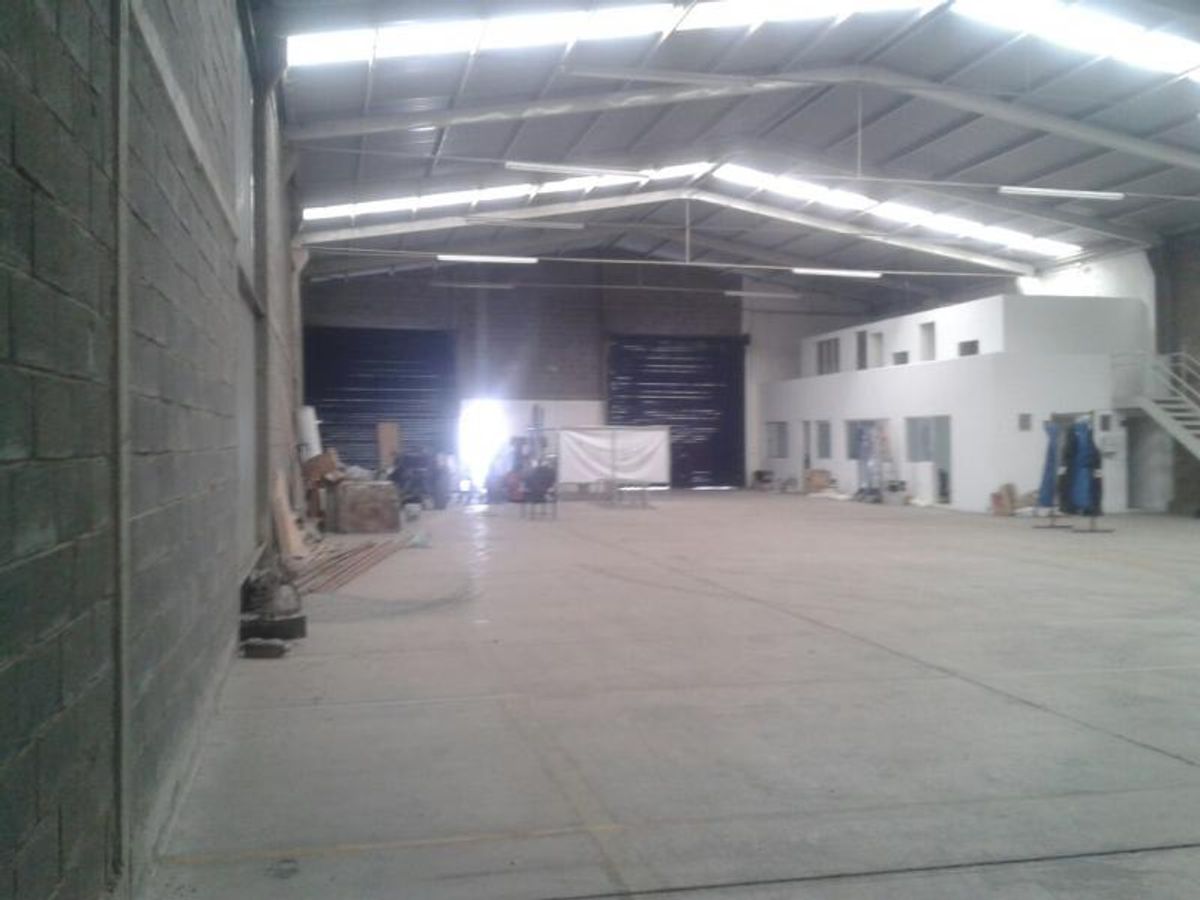 Bodega industrial con piso de concreto, techo metálico con tragaluces y oficinas blancas