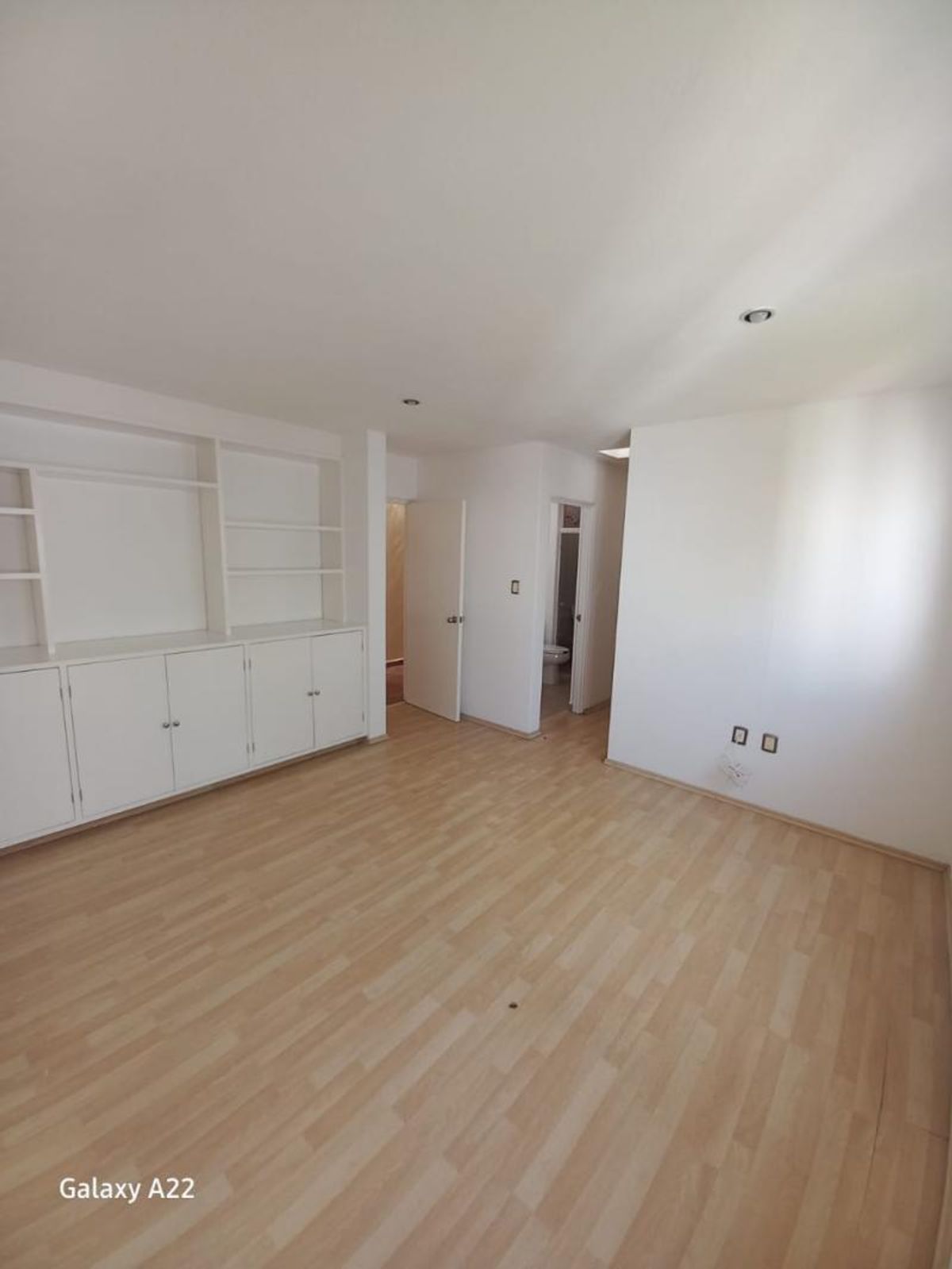 Habitación vacía con piso laminado claro, paredes blancas y mueble empotrado con repisas