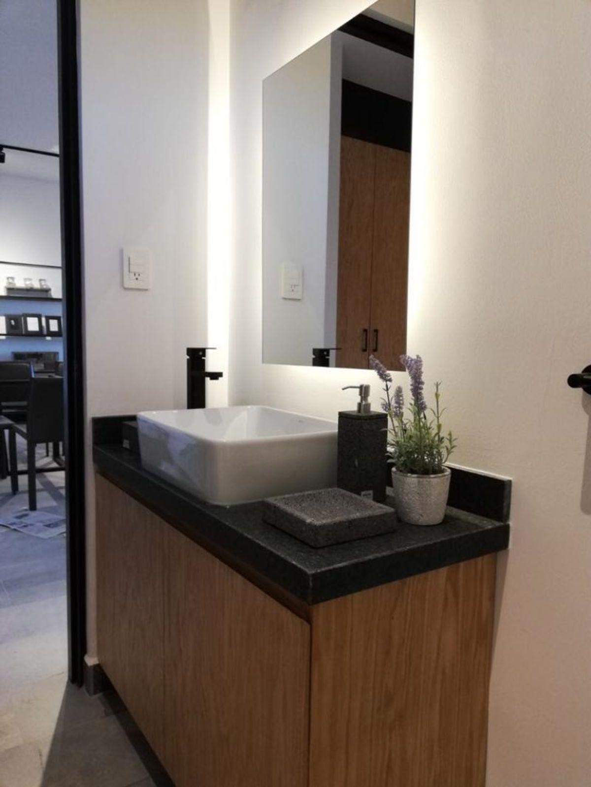 Mueble de baño de madera con cubierta negra, lavabo blanco y espejo retroiluminado