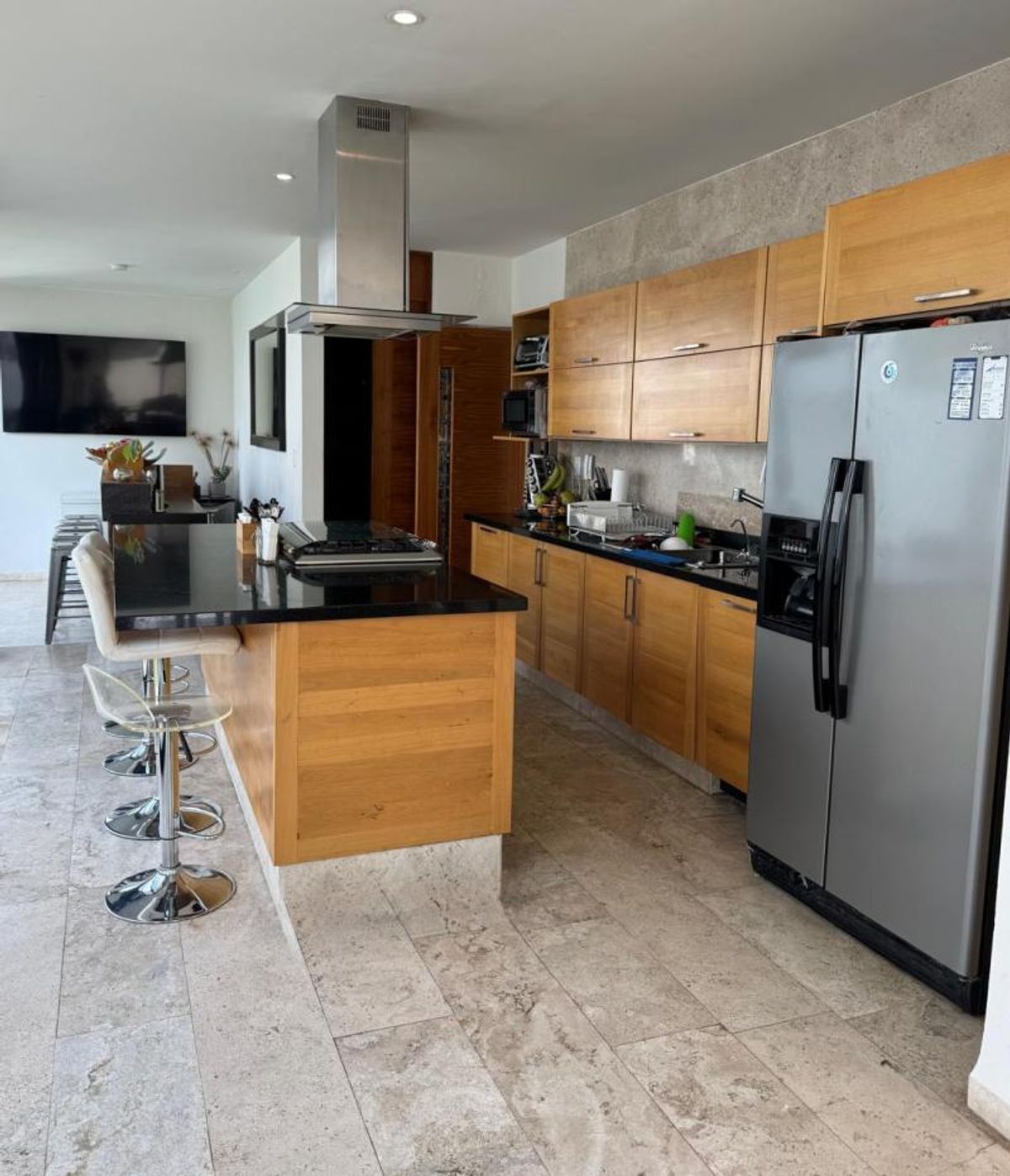Cocina con isla de granito negro, gabinetes de madera y campana de acero inoxidable