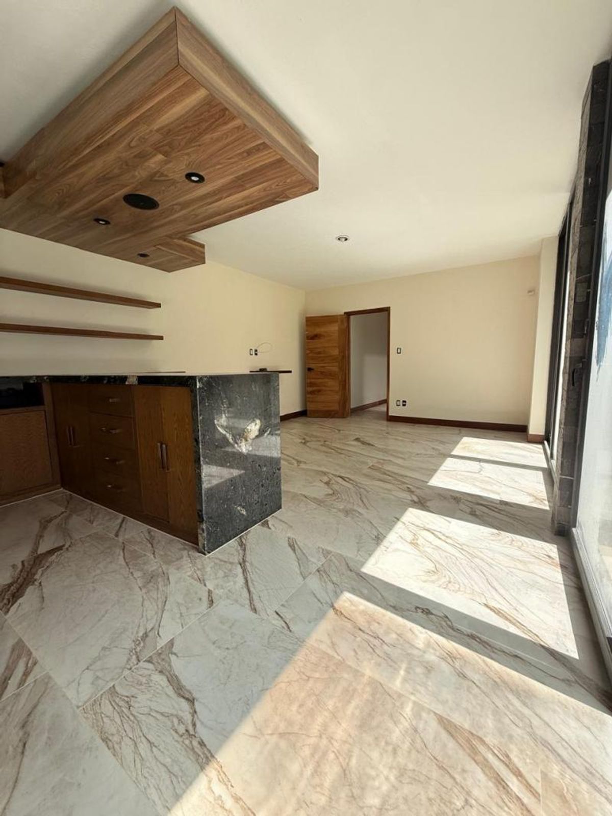 Cocina con barra de granito oscuro, gabinetes de madera, plafón decorativo y piso veteado
