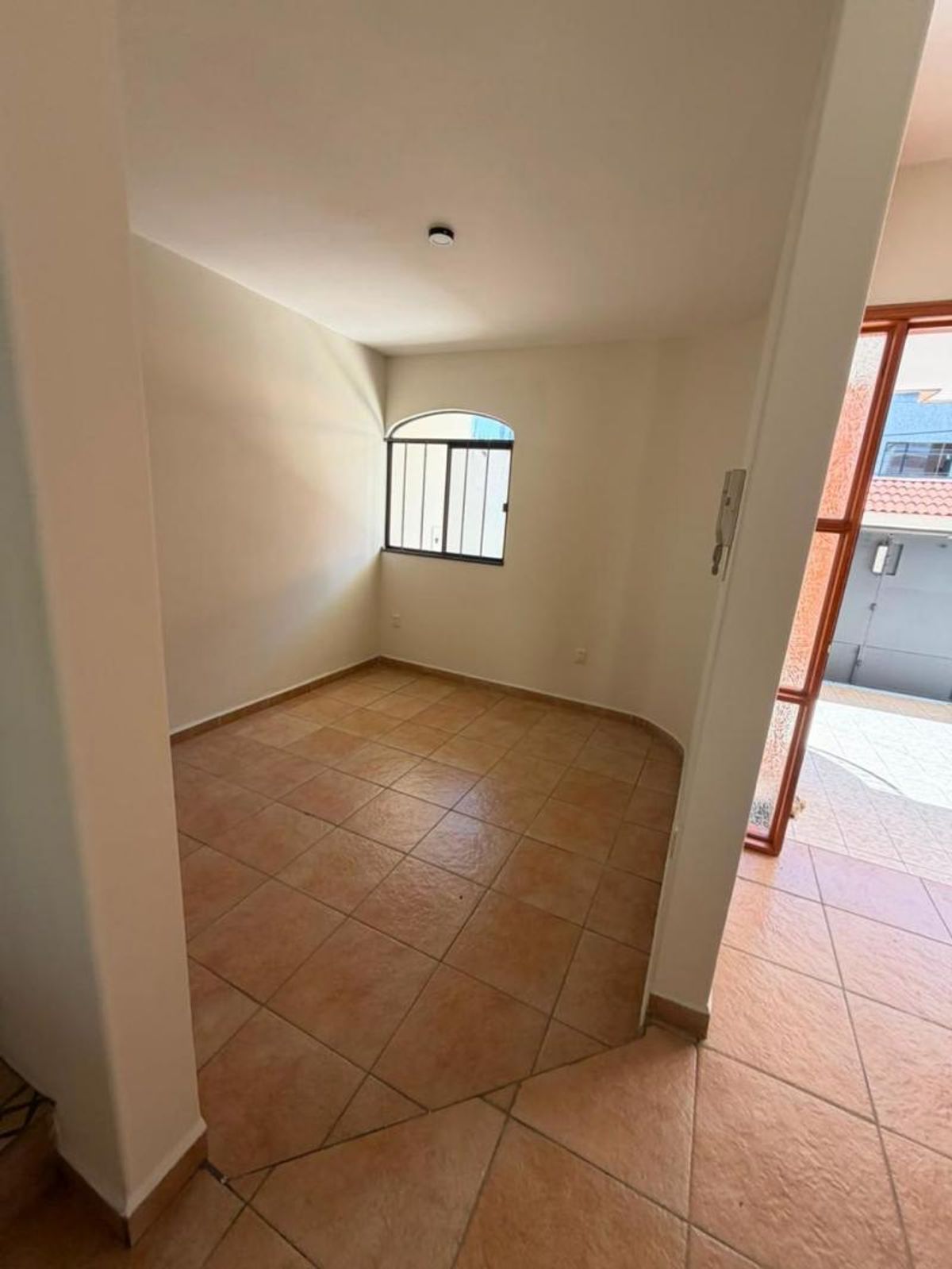 Habitación vacía con piso de azulejo terracota, paredes claras y ventana de marco negro