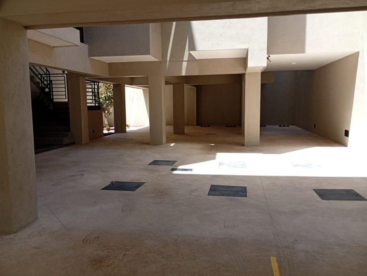 Estacionamiento techado con columnas de concreto, piso con registros metálicos y acceso a escaleras