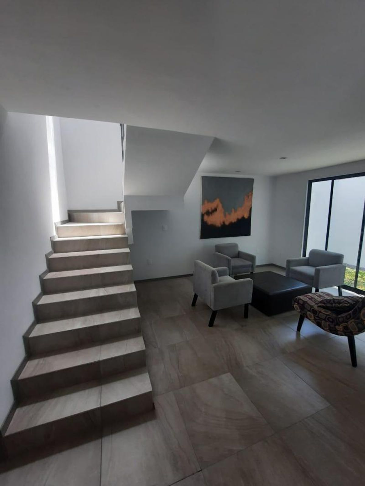 Sala con sillones grises, mesa negra, cuadro en la pared y escalera de cerámica