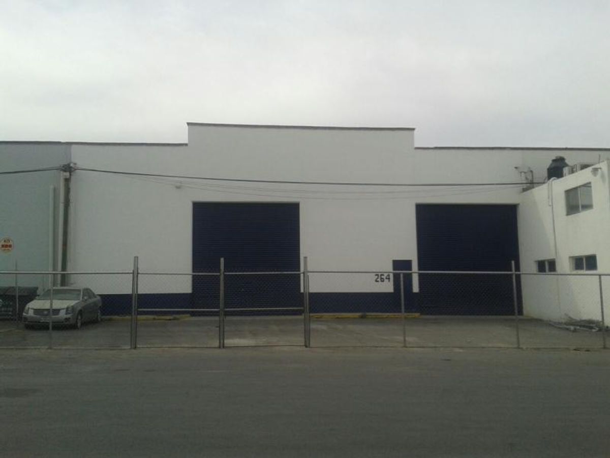 Fachada blanca de bodega industrial con cortinas metálicas oscuras y cercado de malla ciclónica