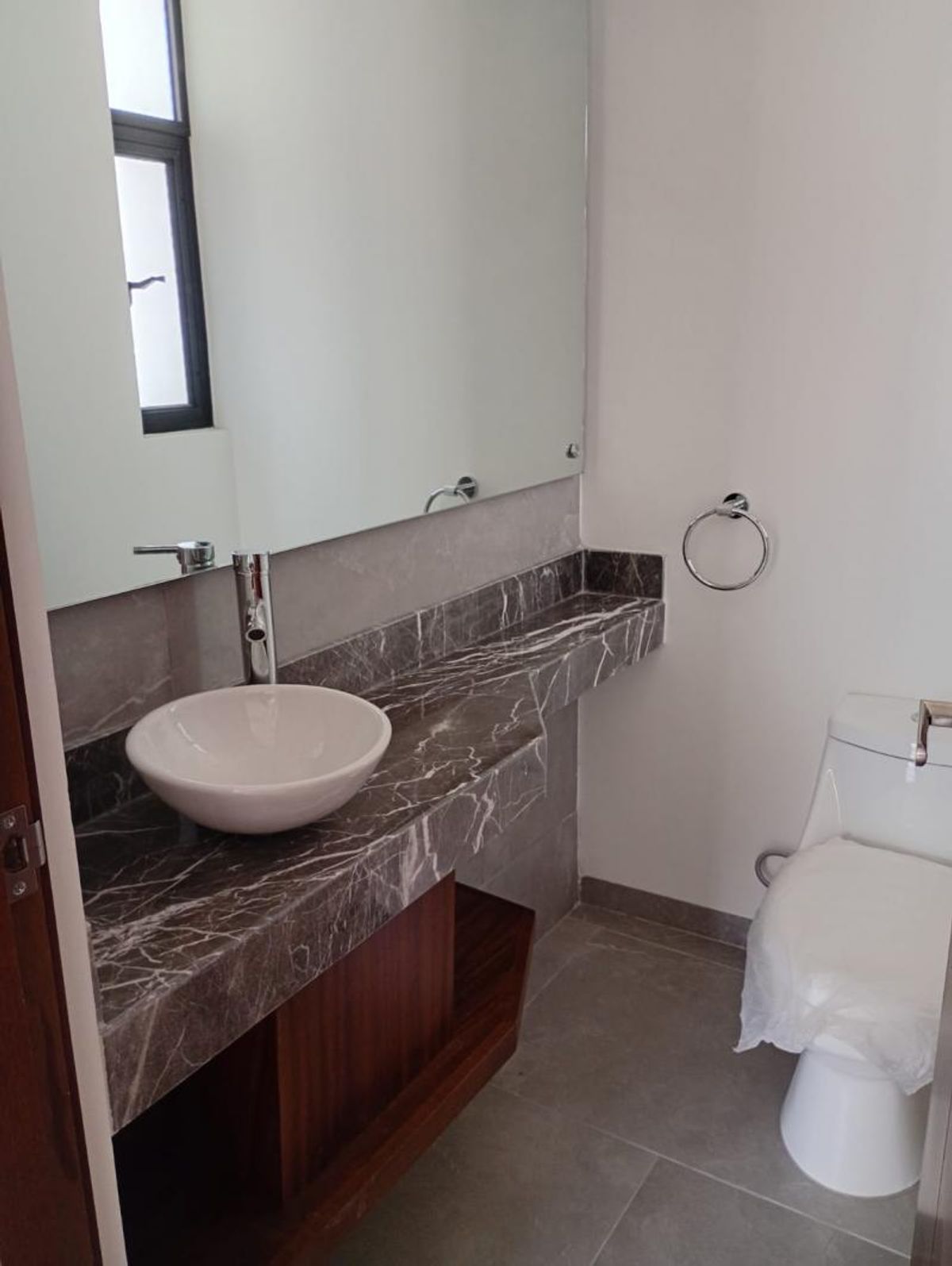 Baño con lavabo blanco sobre cubierta de mármol veteado, mueble de madera e inodoro