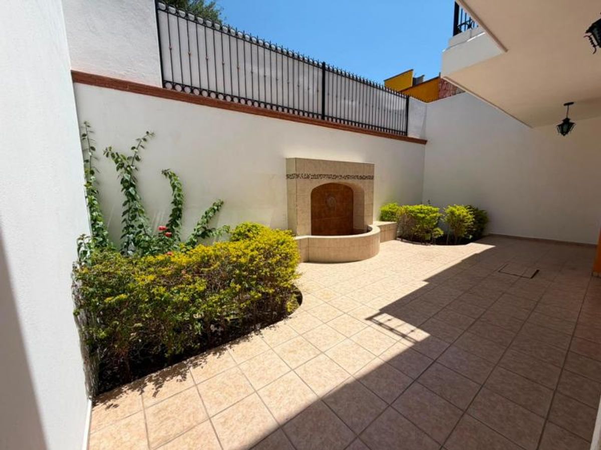 Patio exterior con piso de loseta beige, fuente de piedra y jardineras con plantas