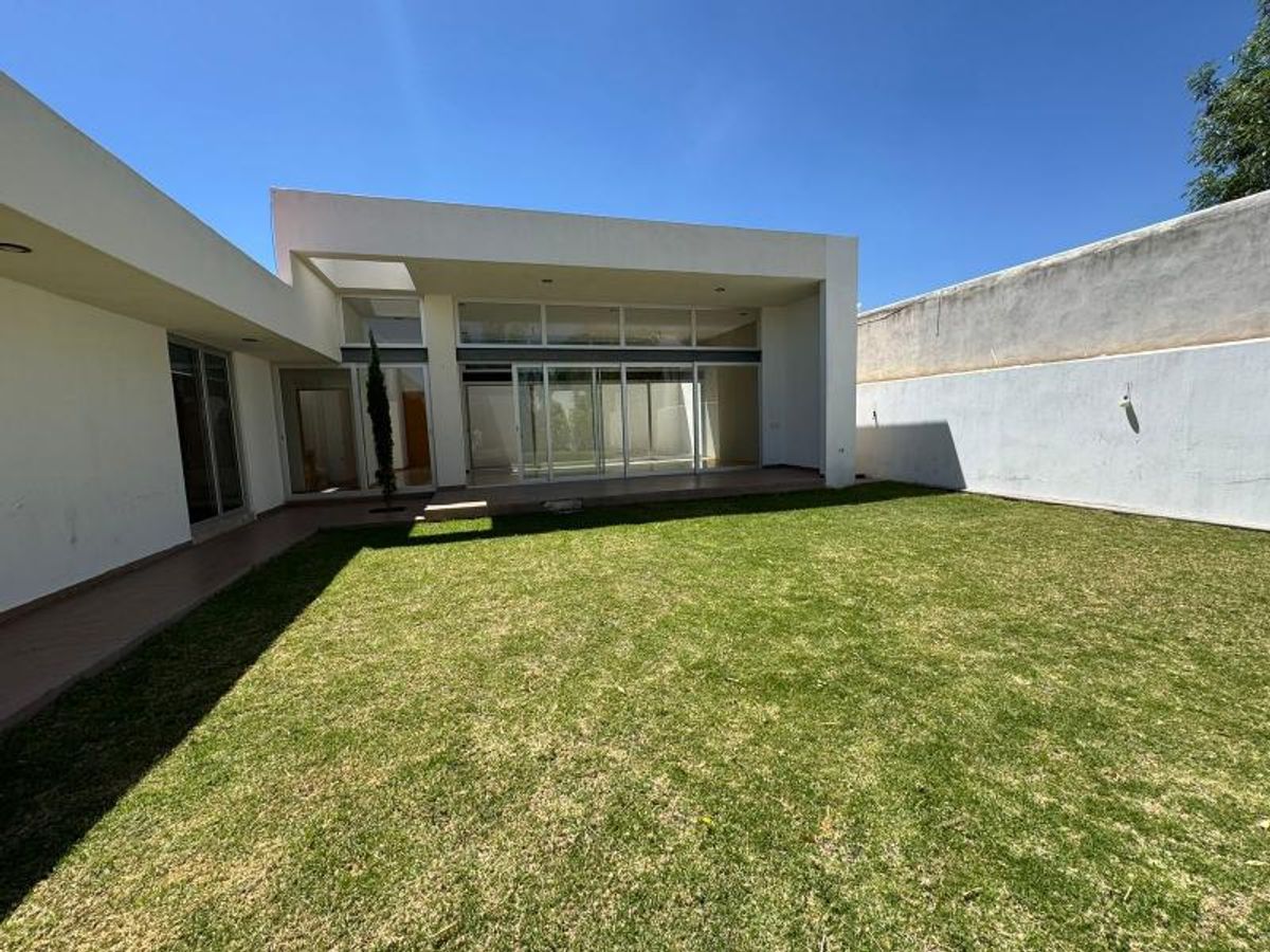 Jardín con césped verde junto a fachada de casa blanca moderna con ventanales de cristal