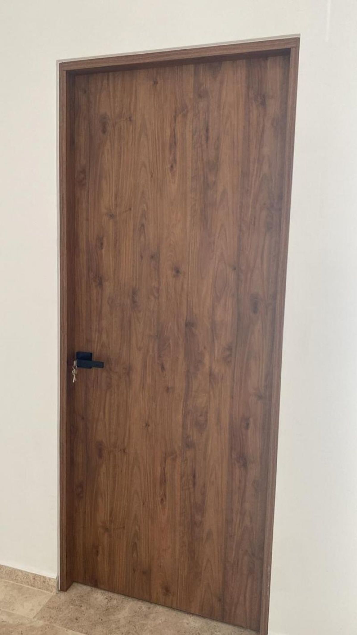 Puerta de madera con veta natural, manija negra moderna y marco en pared blanca