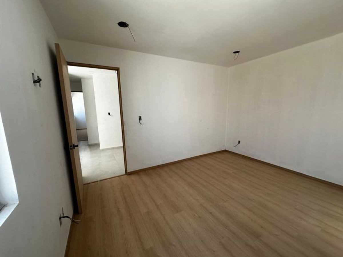 Habitación vacía con piso laminado de madera clara, paredes blancas y puerta de madera abierta