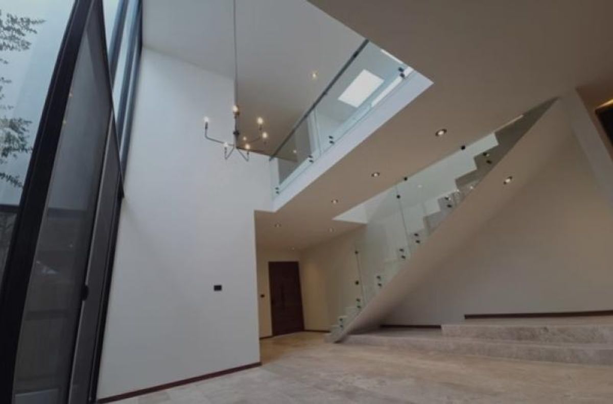Vestíbulo de doble altura con paredes blancas, candelabro colgante y escalera de cristal
