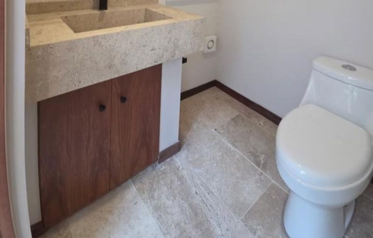 Lavabo de piedra beige con mueble de madera, inodoro blanco y piso de piedra