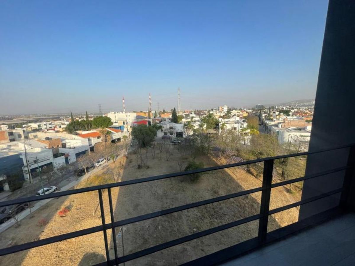 Vista desde balcón con barandal de metal negro hacia terreno y casas residenciales