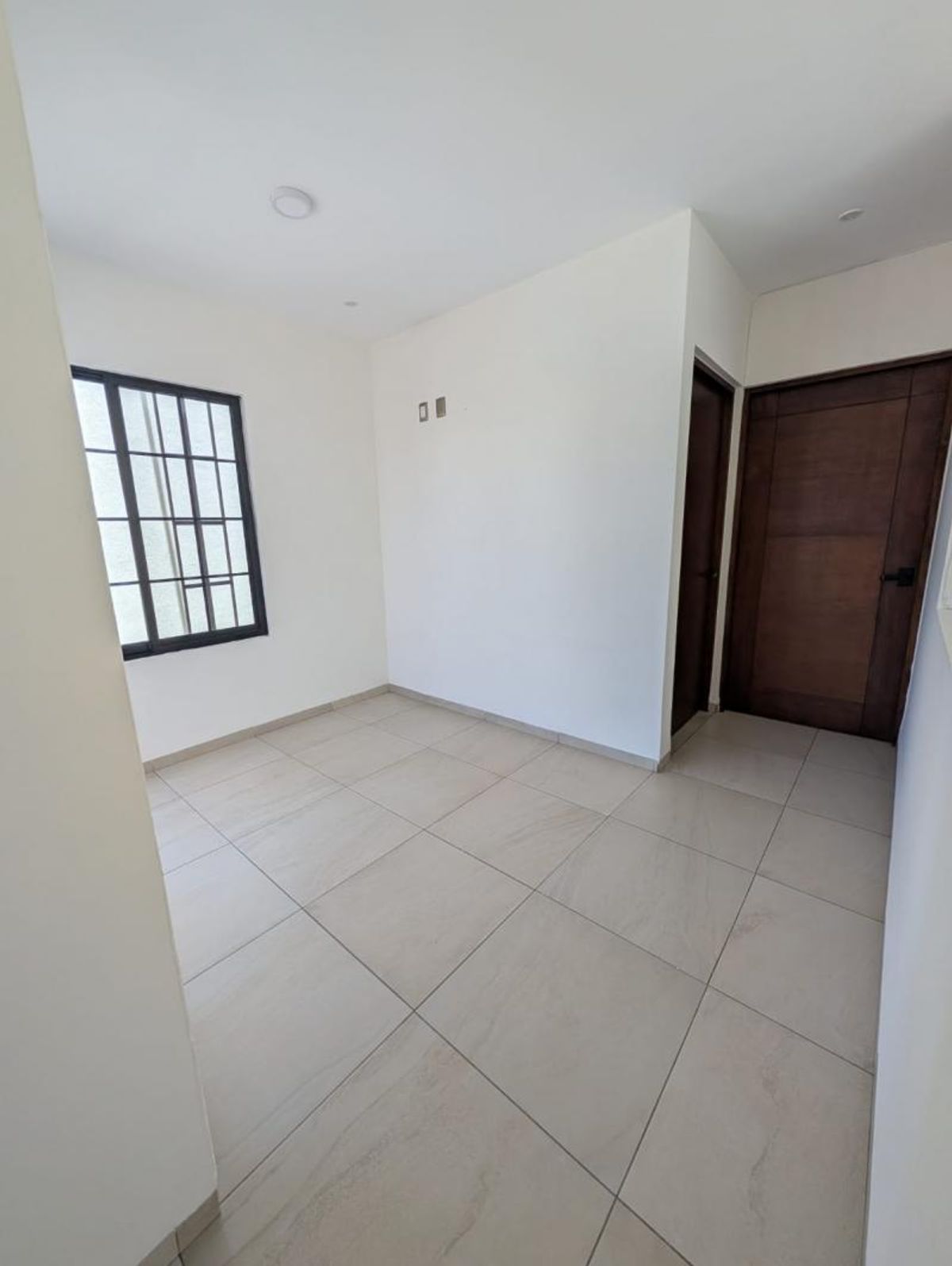 Habitación vacía con piso de cerámica, paredes blancas, ventana negra y puertas de madera