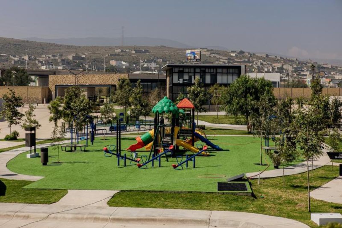 Parque infantil con juegos coloridos, pasto sintético, senderos de concreto y árboles alrededor