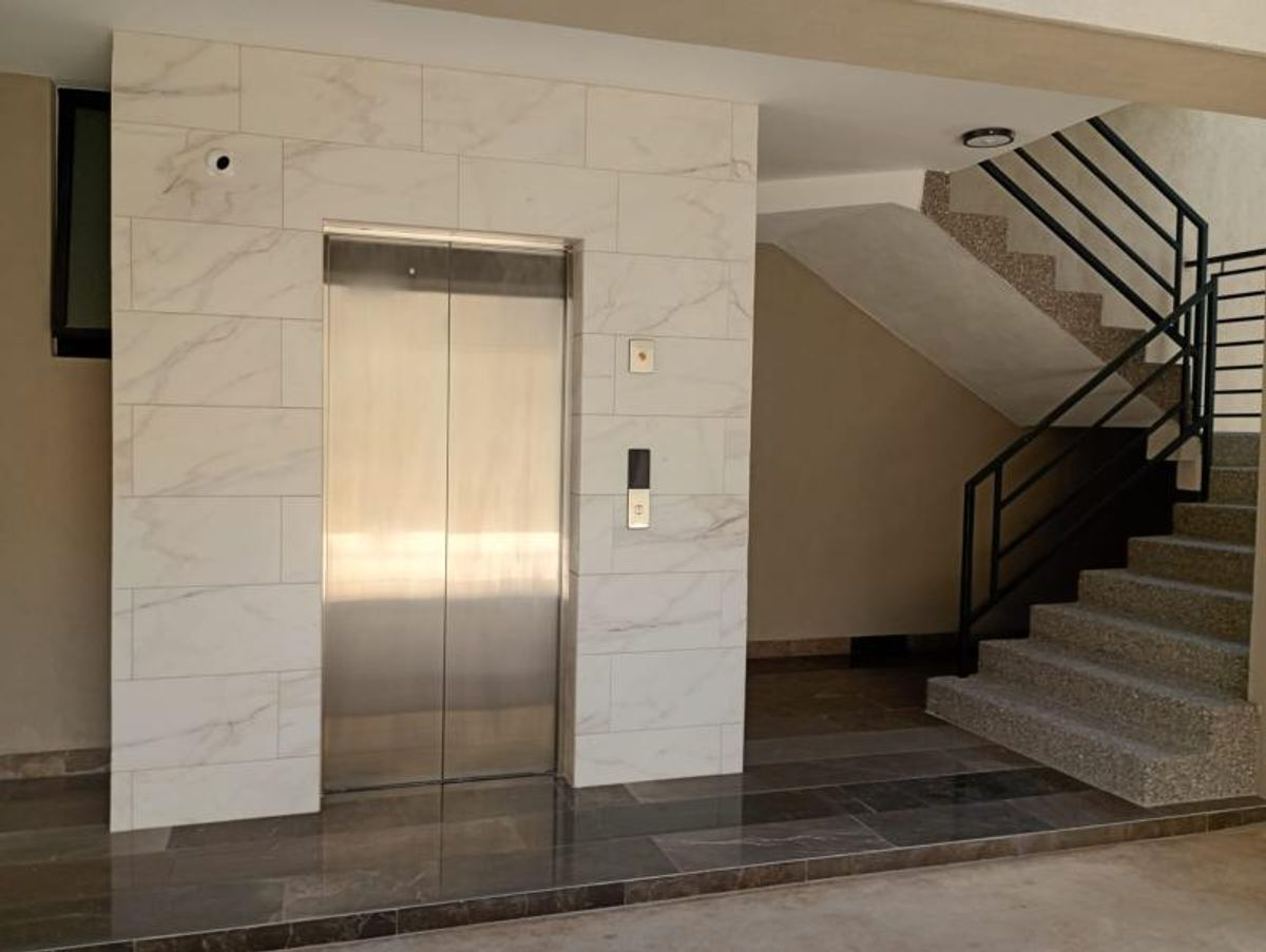 Elevador de acero con revestimiento tipo mármol blanco y escaleras con barandal negro