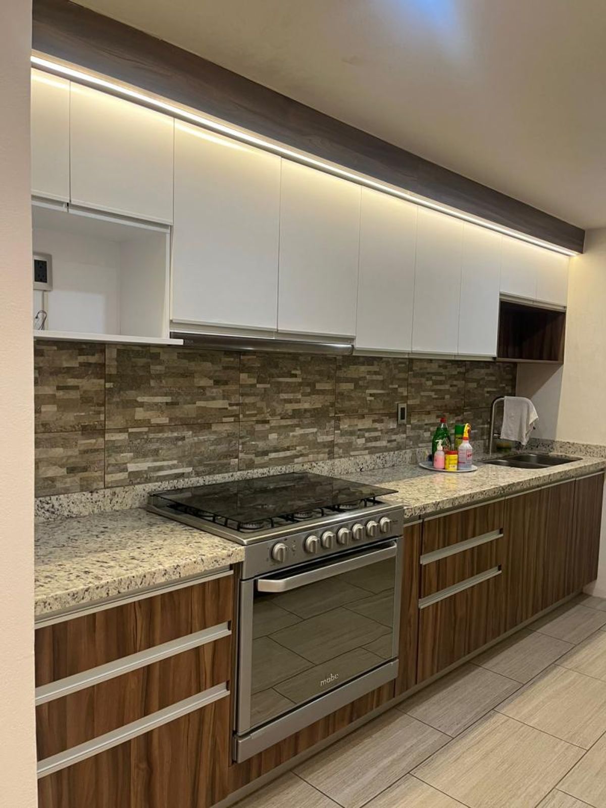 Cocina con gabinetes blancos y de madera, cubierta de granito y estufa de acero