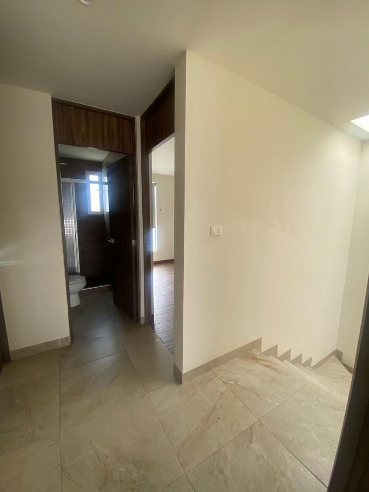 Pasillo con piso de cerámica, marcos de madera oscura y accesos a baño y habitación