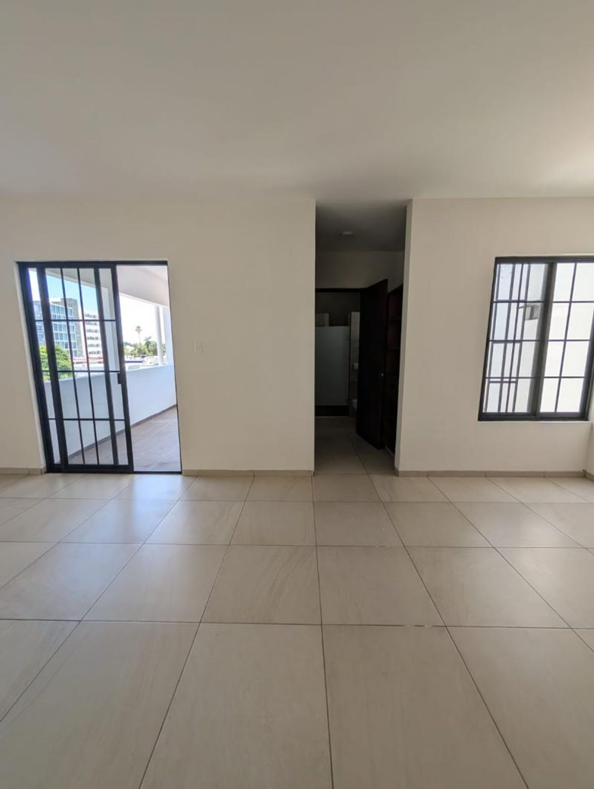Habitación con piso de loseta clara, salida al balcón y ventana con marco negro