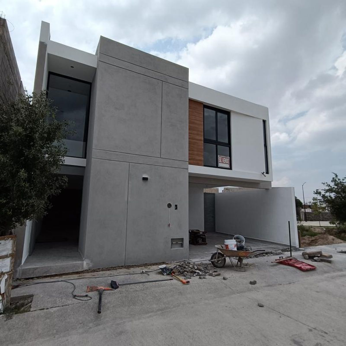 Fachada de dos niveles con concreto gris, muros blancos, panel de madera y ventanales