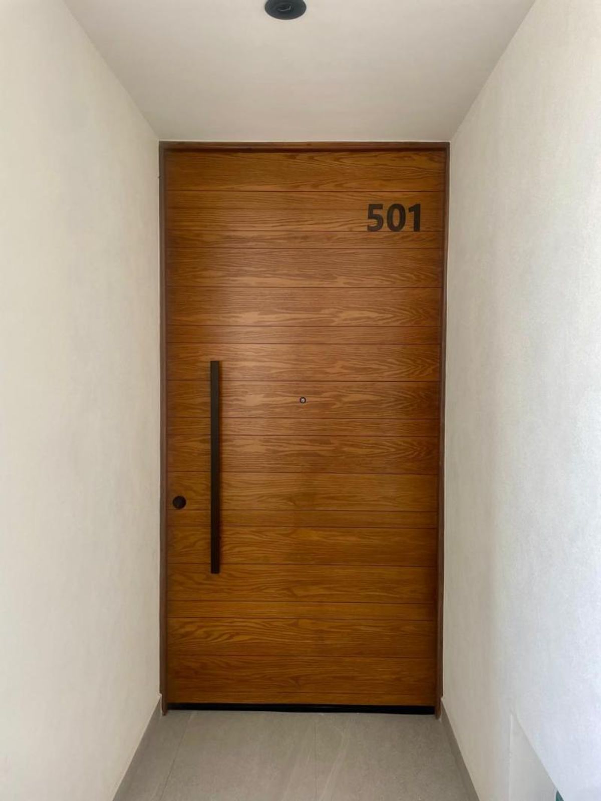 Puerta de entrada de madera con paneles horizontales, jaladera negra vertical y número 501