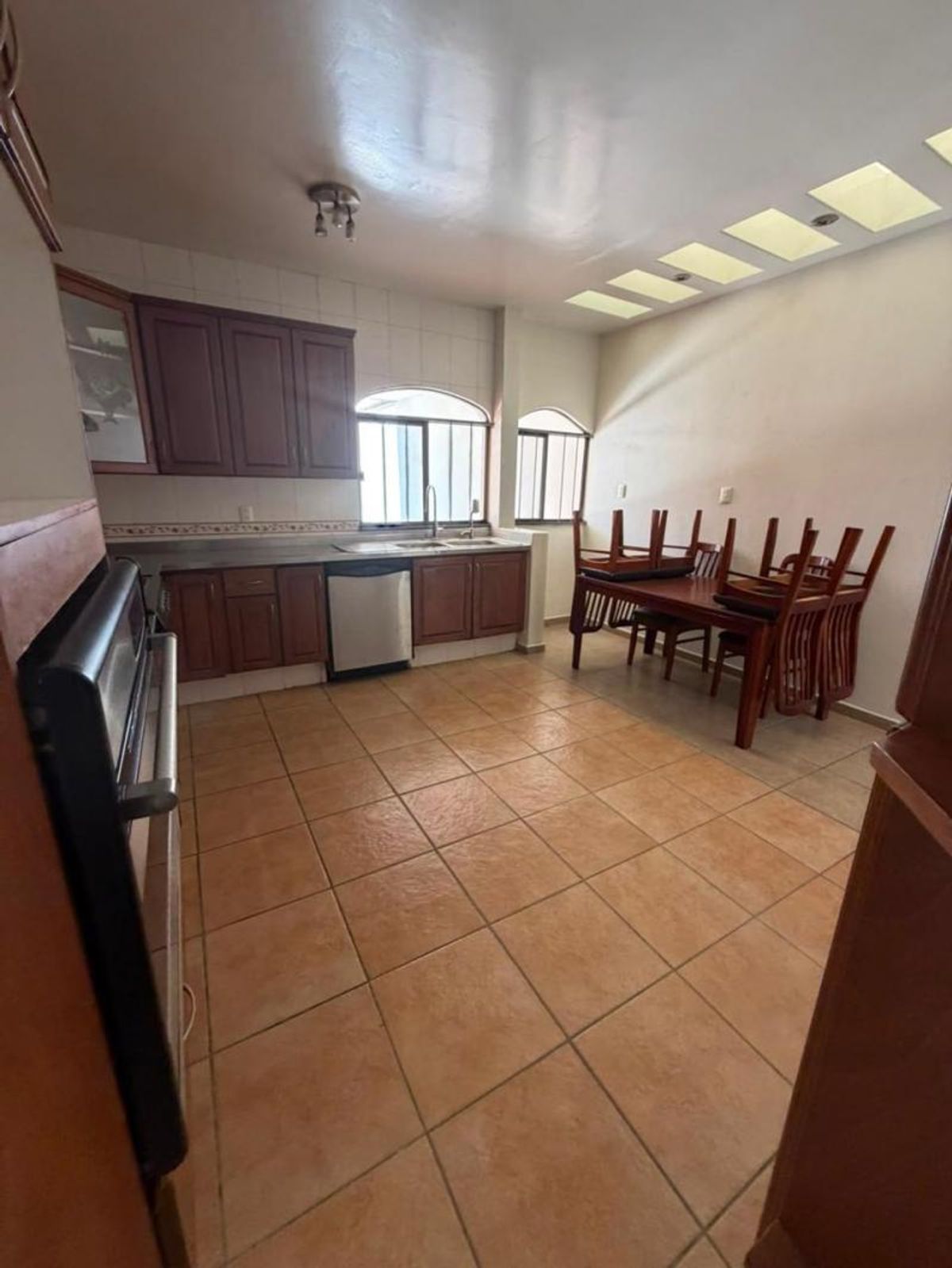 Cocina integral con gabinetes de madera oscura, piso de cerámica y comedor de madera