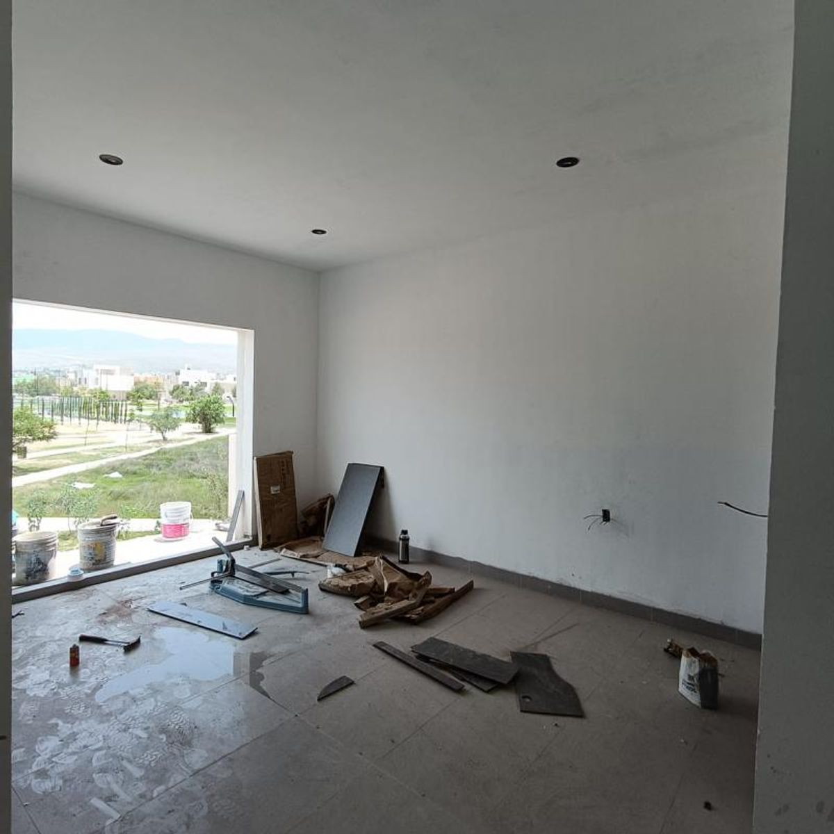 Habitación en construcción con piso cerámico gris, luces empotradas y ventanal hacia el parque