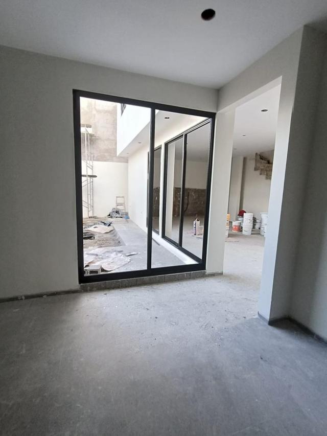 Habitación en construcción con piso de concreto y ventanal de marco negro hacia el patio