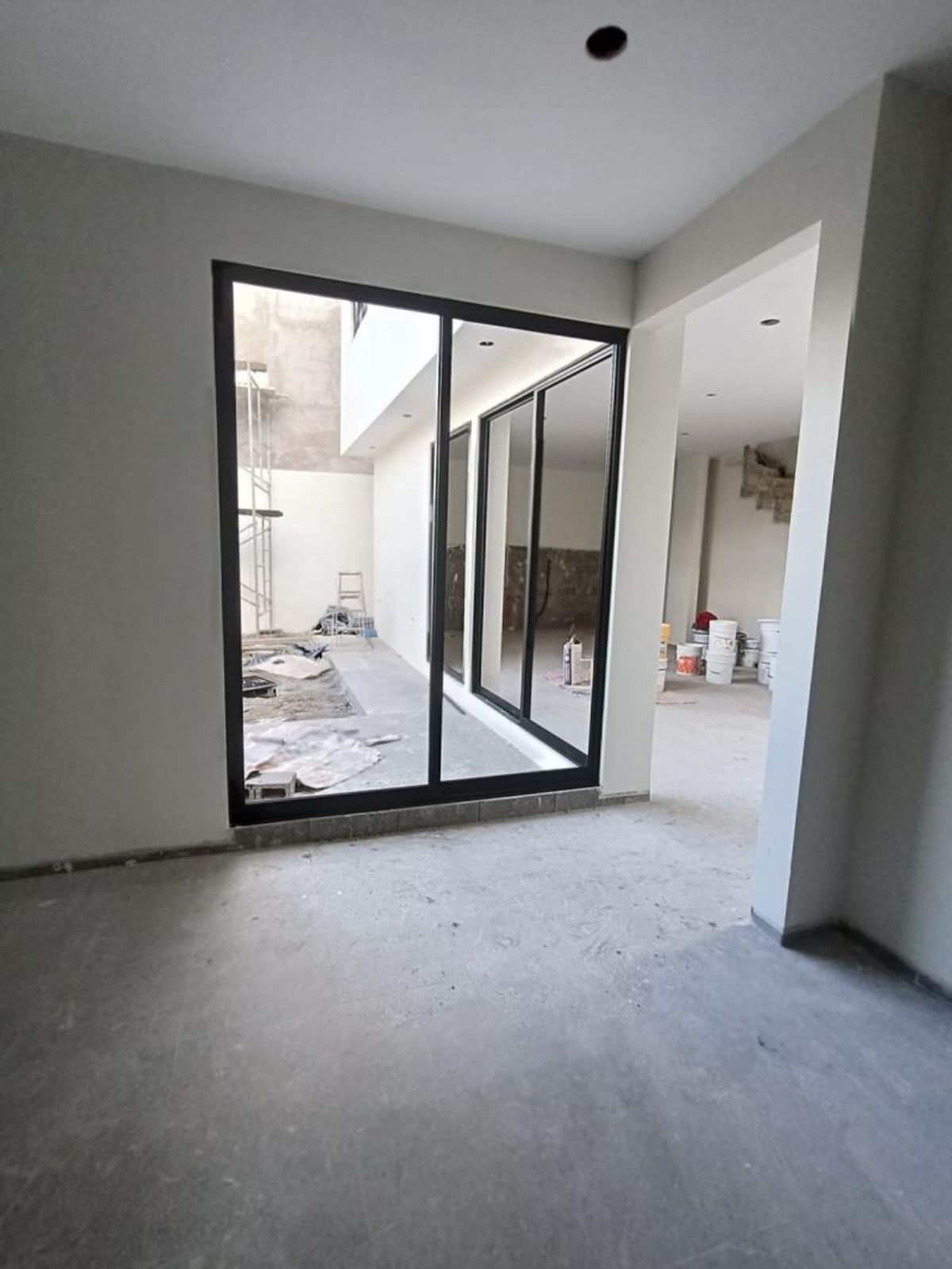 Habitación en construcción con piso de concreto y ventanal de marco negro hacia el patio
