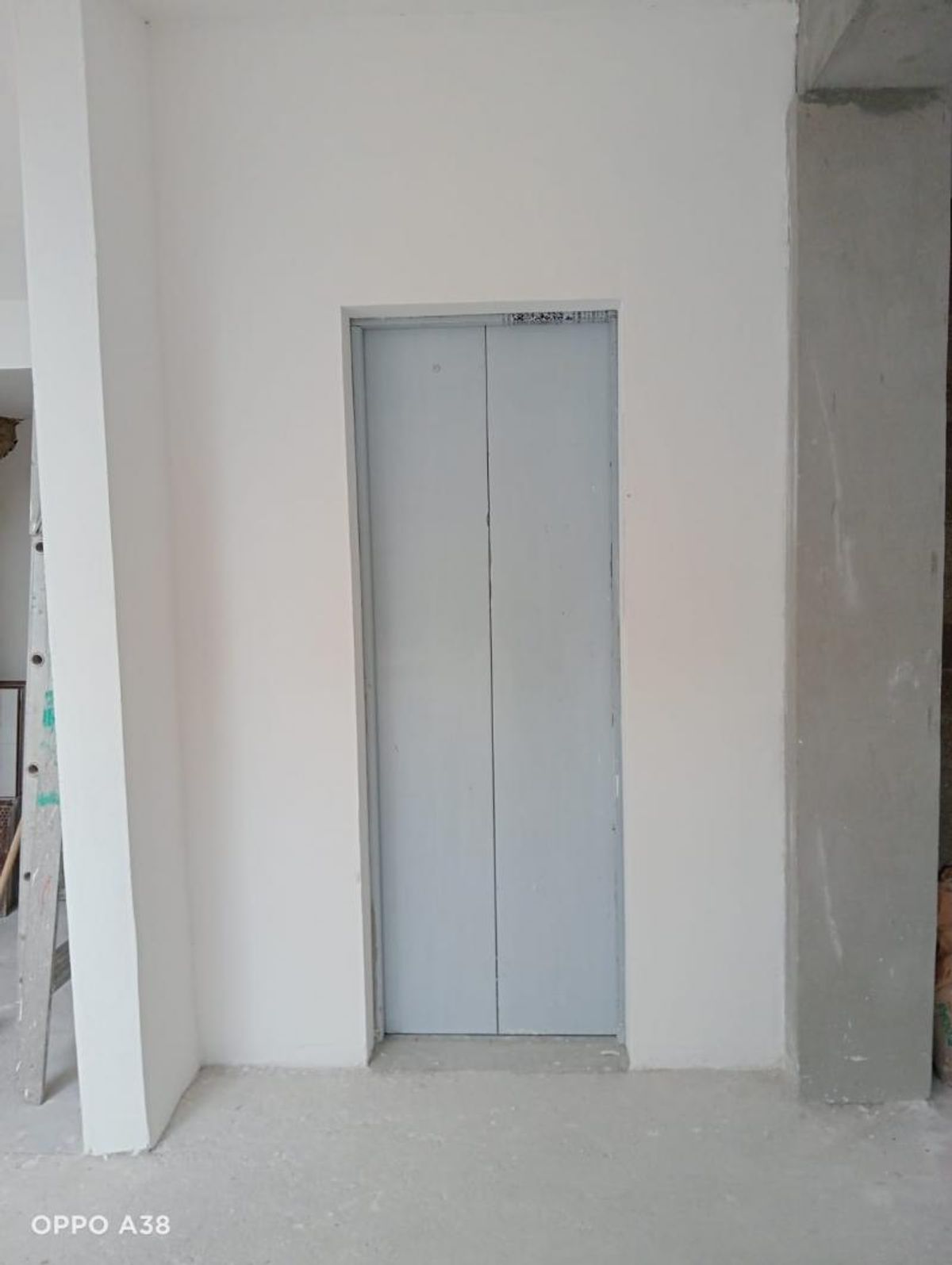 Puerta de elevador de metal gris en pared blanca sobre piso de concreto